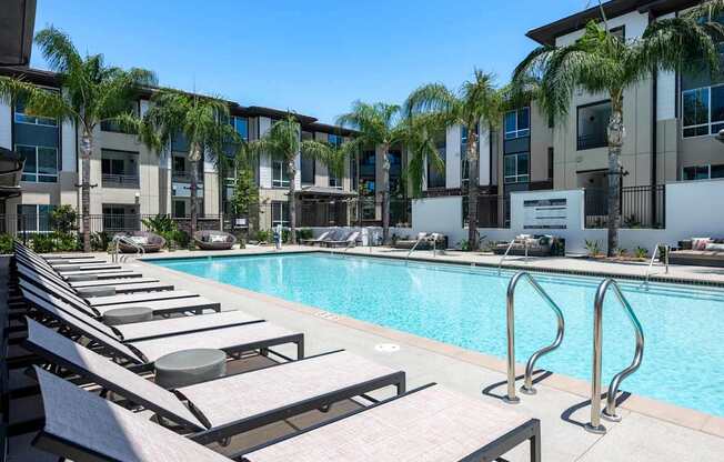 A pool with sun loungers and palm trees in front of a building.