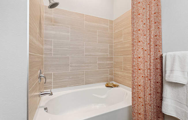 A white bathtub with a shower head and a towel hanging on the wall.