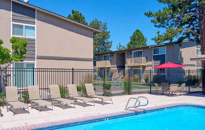 Swimming pool with sun chairs, umbrella-covered seating, surrounded by a fence, apartments, and landscaping.at Wildflower, Kennewick, WA