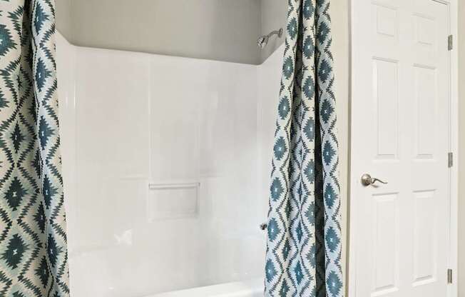 A white door is next to a bathtub with a blue and white shower curtain.