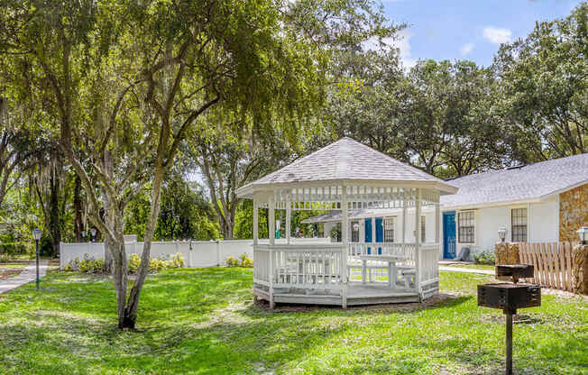 A gazebo is surrounded by a white picket fence and trees.