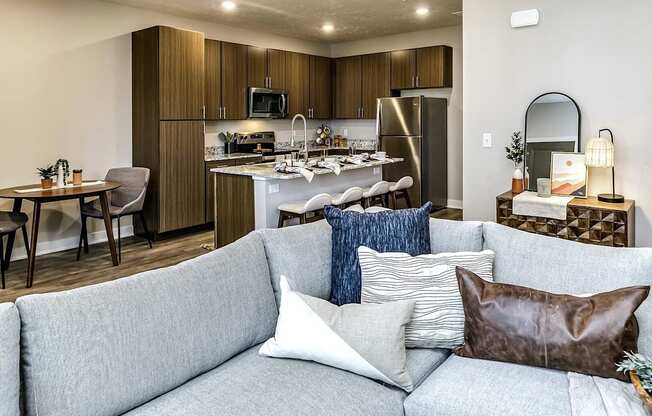 A modern living room with a grey couch and a kitchen in the background.