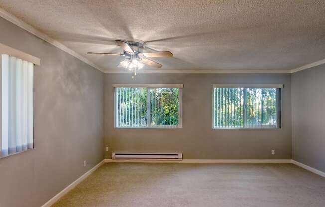 an empty living room with a ceiling fan and two windows