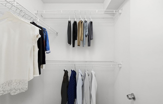 a walk in closet with white walls and a white metal shelf with clothes on it