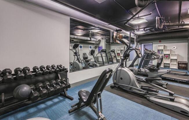A gym with a variety of equipment including dumbbells, weight machines, and a treadmill.