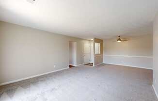 an empty living room with white carpet and a door to a hallway