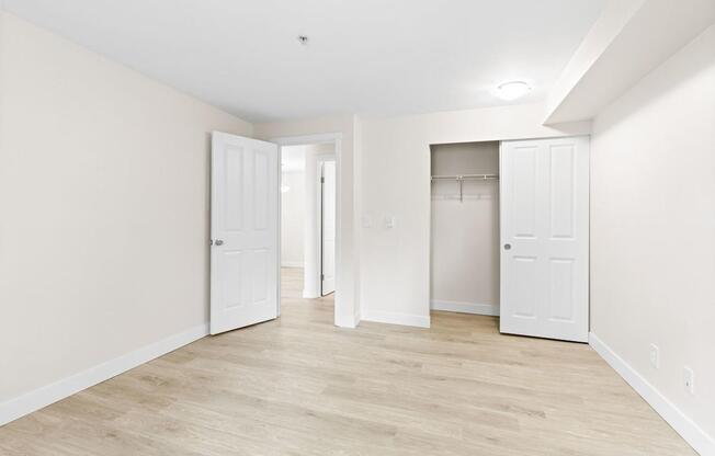 A room with white walls and wooden flooring with two white doors.