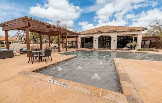A pool with a wooden pergola and a house in the background.