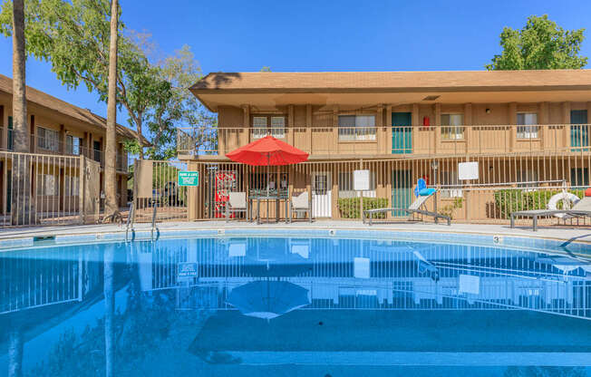 A swimming pool in front of a building with a red umbrella.