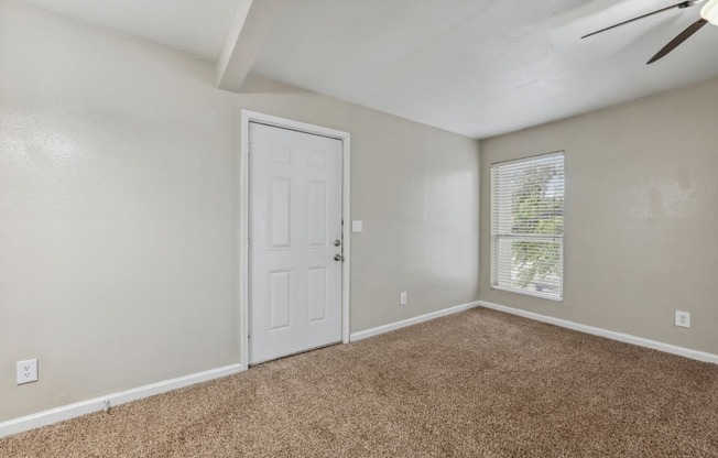 an empty living room with a white door and a window