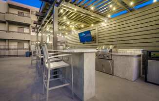 the outdoor kitchen has a bar with chairs and a television