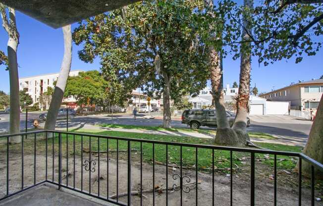 the view of a street from a balcony with a fence and trees