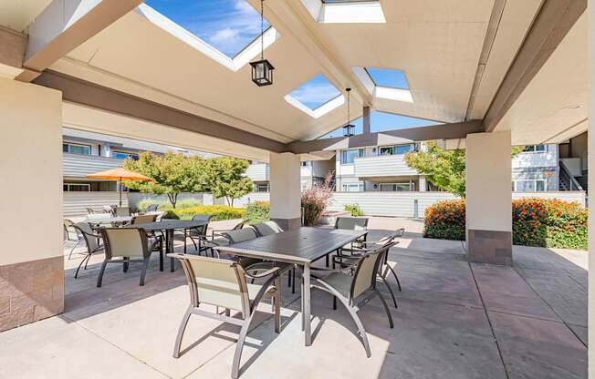A patio with a table and chairs under a roof with skylights.