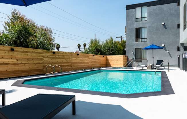 a pool in a backyard with a wooden fence and a gray building in the background