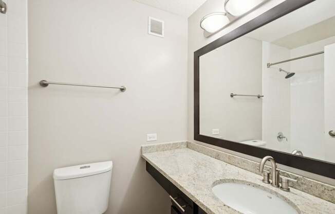 A bathroom with a toilet, sink, mirror and towel rack.