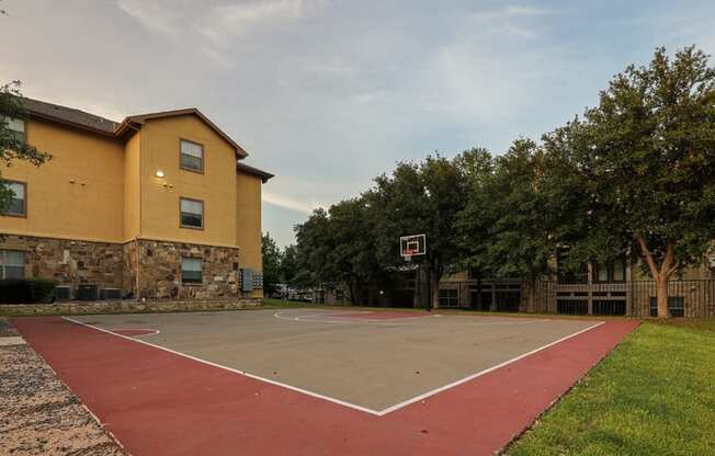 a basketball court in front of a yellow building with trees