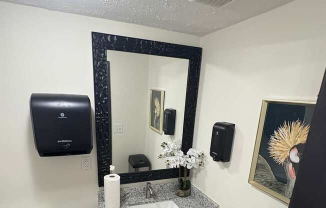 A bathroom with a toilet, sink, mirror, and a painting on the wall.