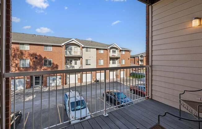 A balcony with a metal railing and a few cars parked in the parking lot.