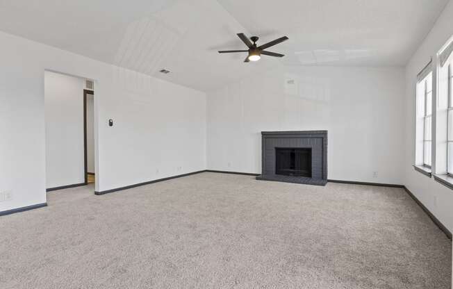 an empty living room with a fireplace and a ceiling fan