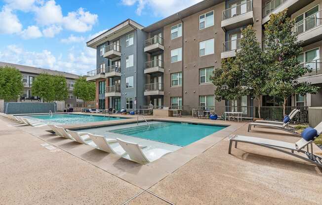 A large apartment complex with a pool and sun loungers.