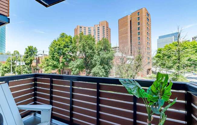 A balcony with a chair and a potted plant overlooking a cityscape.