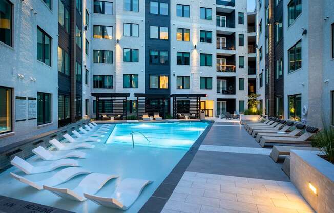 A swimming pool surrounded by lounge chairs in front of a building.