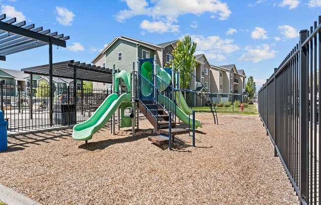 A playground with a green slide and a brown ground.