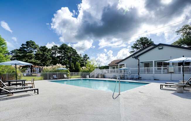 A swimming pool surrounded by a concrete patio and a white house.