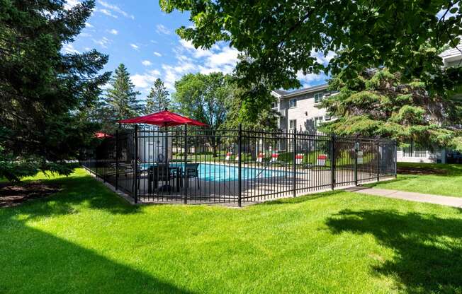 a fenced in pool with a table and umbrella in a yard