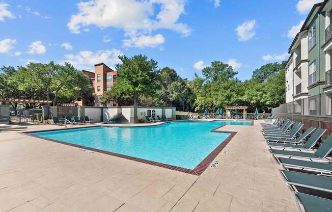 A large outdoor swimming pool surrounded by lounge chairs and trees.