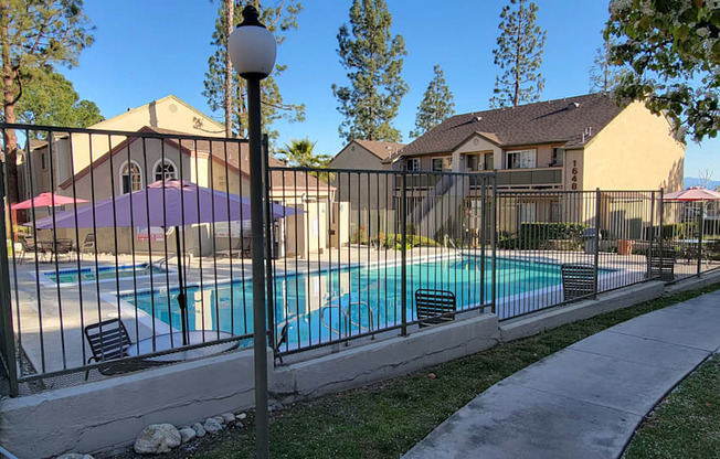 Gated swimming pool, spa, and sun deck area surrounded by lush gardens and trees at Northwood Apartments in Upland, California.