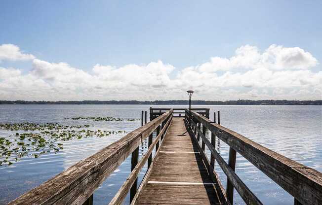 A wooden pier extends into a body of water with a cloudy sky above.