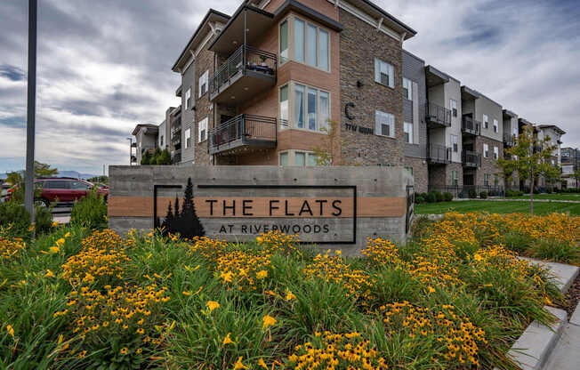 the flats at riverwoods apartments sign in front of grass and flowers