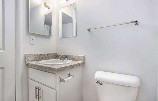 A bathroom with a white cabinet, sink, mirror, toilet and towel bar at Brookside Apartments, Springfield