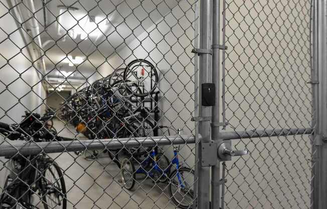 A chain link fence with a gate is in front of a wall with a bunch of bicycles hanging on it.