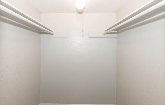 An empty closet featuring two hanging rods against plain light-colored walls. The ceiling has a single overhead light fixture providing illumination. The floor is carpeted.