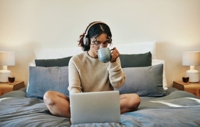 woman at home drinking coffee and on laptop in bed