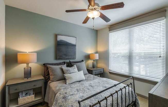 A bedroom with a bed, two lamps, and a ceiling fan.