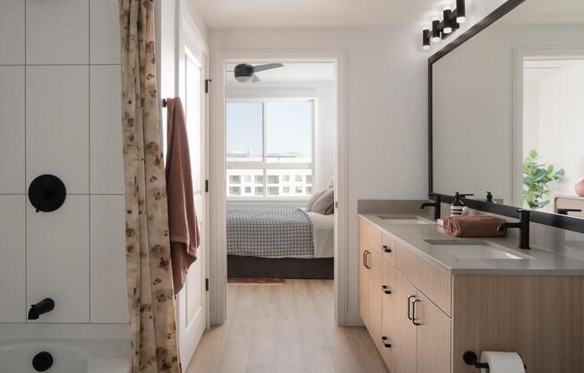 A bright bath with dual sinks, matte black fixtures, and a seamless flow into the bedroom beyond.