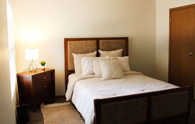 a bedroom with a bed with white bedding and a nightstand with a lamp on it