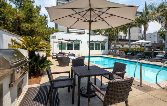 A patio with a table and chairs under an umbrella next to a pool.