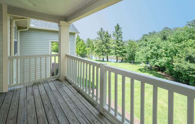 A wooden porch with a view of a green lawn and trees.