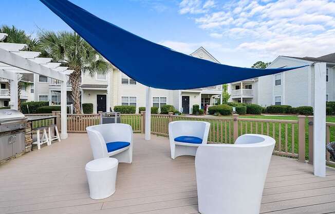 A blue shade sail over a white patio furniture set.