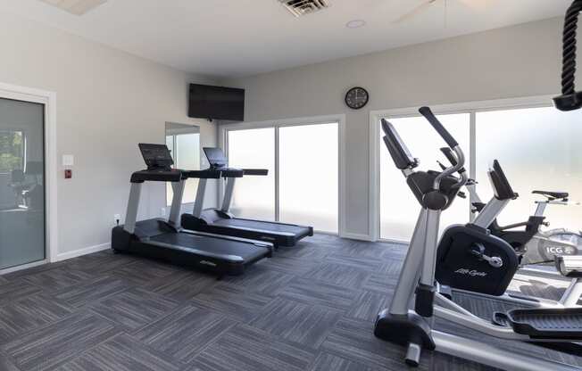 two treadmills and a tv in a gym room with windows