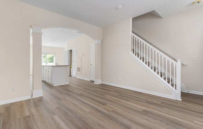 an empty living room with a staircase and a kitchen