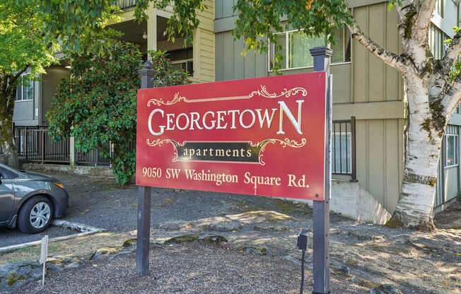A red sign that says Georgetown Apartments stands in front of a building.