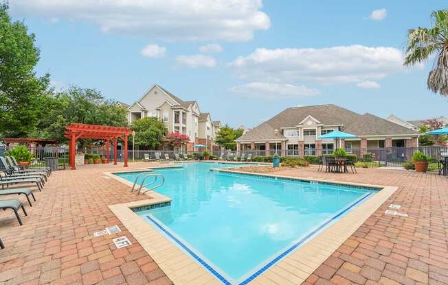A swimming pool surrounded by a brick patio and lounge chairs.