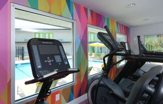 Fusion Las Vegas fitness center with colorful geometric wall and ellipticals looking out large windows toward community pool.