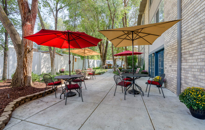 a patio with tables and umbrellas in front of a brick building