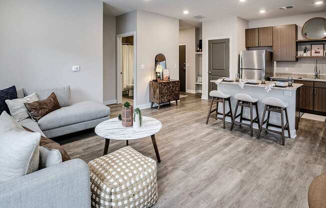 A modern living room with a grey sofa, a white coffee table, and a kitchen area in the background.